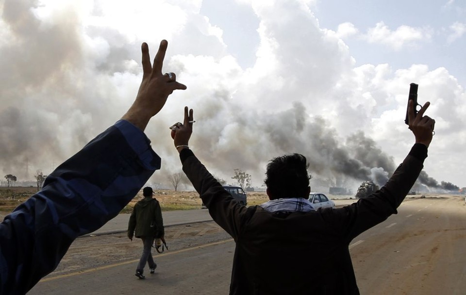 Rebeldes vibram diante de veículos em chamas, pertencentes às forças de Muamar Kadafi, numa estrada entre Benghazi e Ajdabiyah | Goran Tomasevic/Reuters