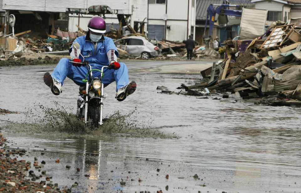 Homem anda de motocicleta entre escombros e água na cidade de Ishinomaki, após réplica de terremoto que matou 2 pessoas no Japão na quinta-feira (7) | TOPSHOTS AFP PHOTO / JIJI PRESS
