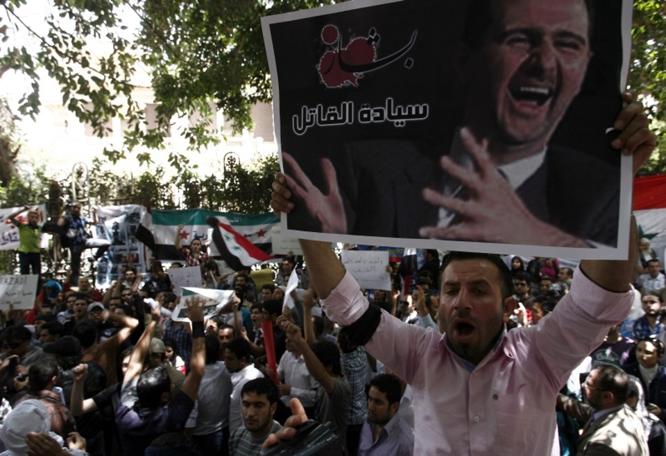 Manifestante exibe cartaz com imagem do presidente sírio Bashar al-Assad em frente à embaixada síria no Cairo | AFP