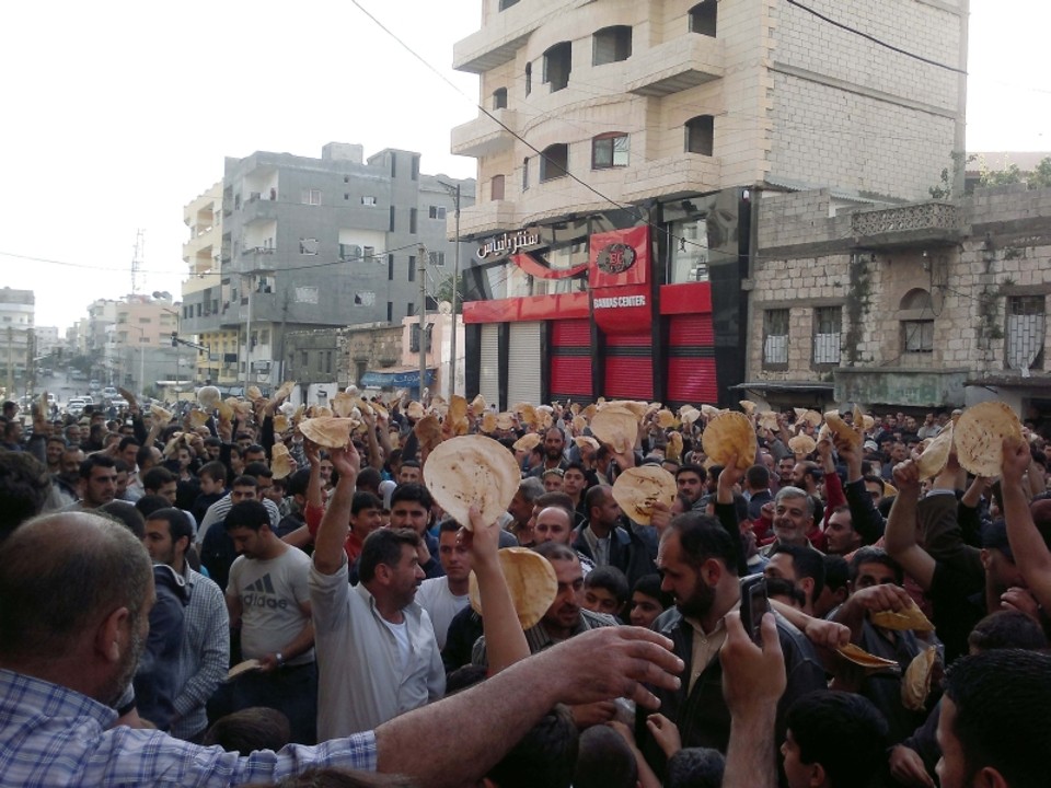 Manifestantes seguram pedaços de pão demonstrando solidariedade aos protestos em Deraa, na cidade de Banias | Reuters
