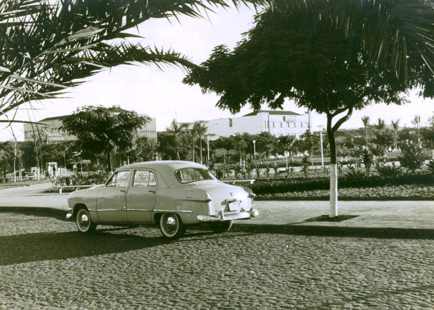 Imagem da década de 1960, após a reurbanização. Na foto aparecem a Avenida Duque de Caxias, ainda formada por paralelepípedos, com a praça como pano de fundo. Em destaque, um Ford 1951 Custom 4 portas. Mais atrás, aparecem o Hotel Aliança, a Caixa Econômica Federal, a Prosdócimo e a Hermes Macedo | 