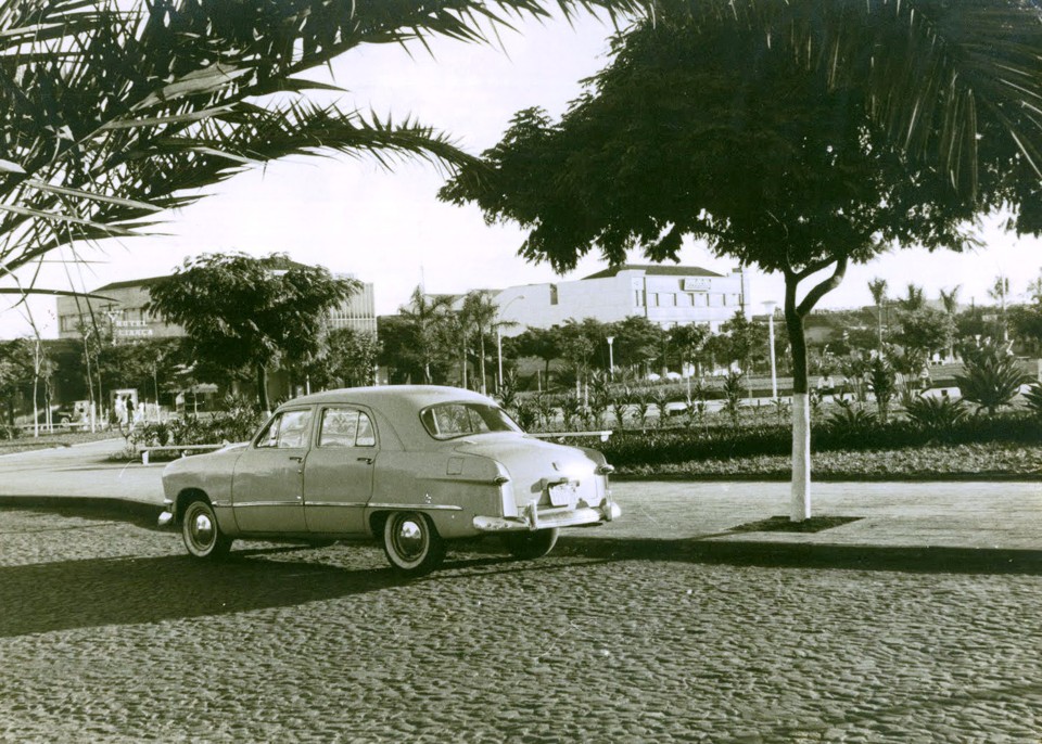 Imagem da década de 1960, após a reurbanização. Na foto aparecem a Avenida Duque de Caxias, ainda formada por paralelepípedos, com a praça como pano de fundo. Em destaque, um Ford 1951 Custom 4 portas. Mais atrás, aparecem o Hotel Aliança, a Caixa Econômica Federal, a Prosdócimo e a Hermes Macedo |
