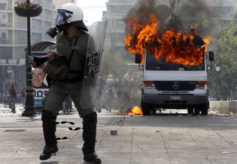 Policial se defende perto das chamas de um caminhão durante os protestos na Praça Syntagma, em Atenas | Reuters