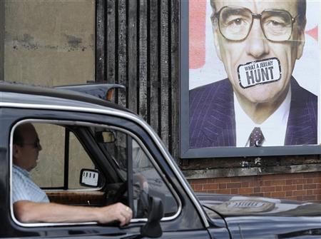 Táxi passa em frente a um cartaz assinado pelo artista Dr. D com um retrato de Rupert Murdoch, chefe da News Corp., em Londres | Reuters