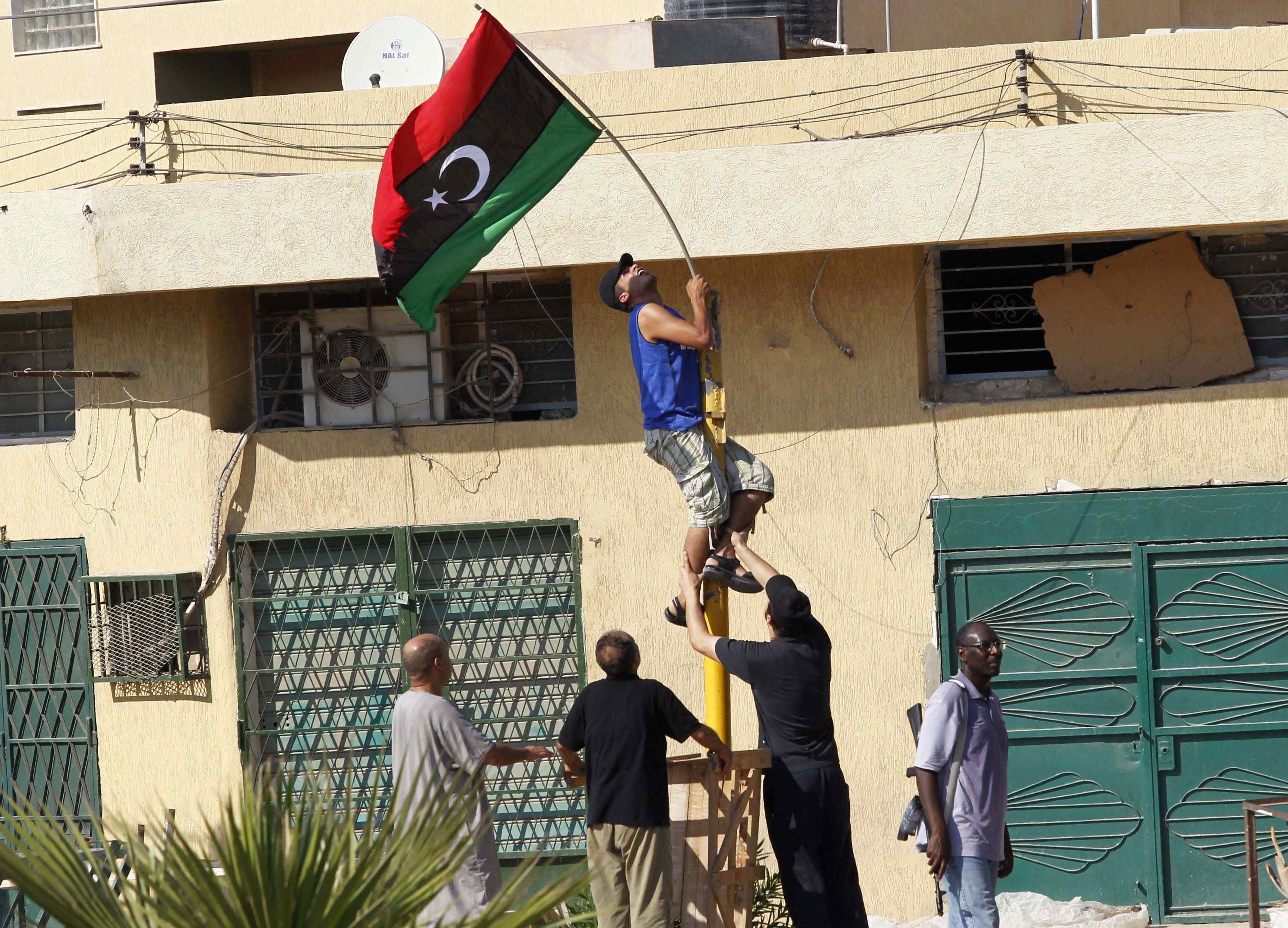 Rebelde hasteia bandeira do reino da Líbia um dia depois da tomada do complexo de Muamar Kadafi em Trípoli | REUTERS/Louafi Larbi