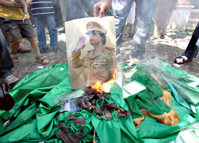 Simpatizantes dos insurgentes líbios queimam cartazes com foto de Kadafi e bandeiras do regime | Reuters