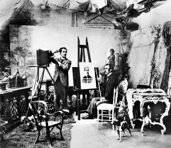 Olha o passarinho. Atualmente todo mundo é fotógrafo graças ao desenvolvimento tecnológico das câmeras fotográficas e de seu custo barateado. No século passado a coisa era diferente. Fotografia era feita em estúdio. Famílias, grupos de amigos, casamentos, batizados e mais quem quisesse guardar imagens à posteridade tinha que ir ao retratista de estúdio. Lá havia de tudo, móveis, cenários e até cachorros empalhados para fazerem parte da cena. Na foto vemos os irmãos Weiss em seu atelier na Rua da Liberdade, (Barão do Rio Branco), por volta de 1900 | 