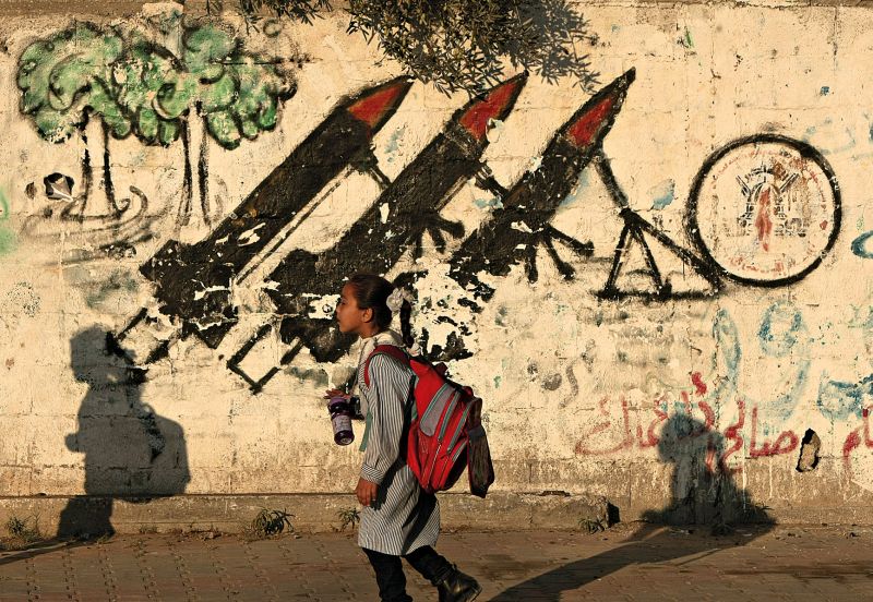 Estudante palestina passa em frente de muro com desenhos sobre o conflito, em Gaza, região governada pelo grupo radical Hamas | Mahmud Hams/AFP