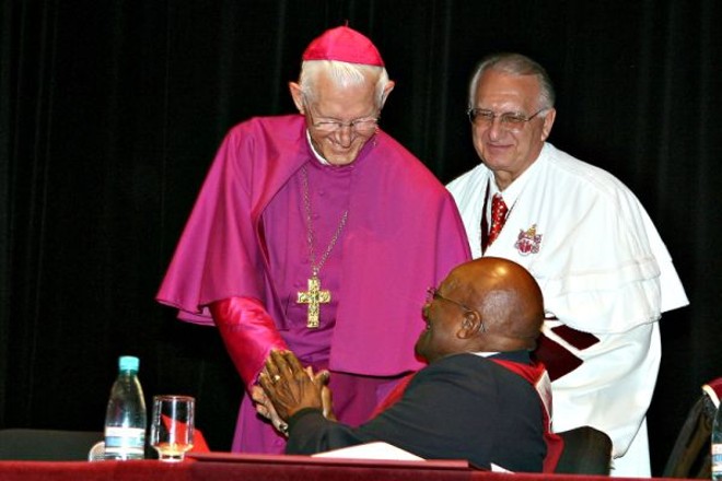 Desmond Tutu é cumprimentado pelo arcebispo metropolitano de Curitiba, dom Moacyr Vitti, observado pelo reitor, que classificou o evento como um dia histórico para a Pontifícia Universidade Católica do Paraná | 