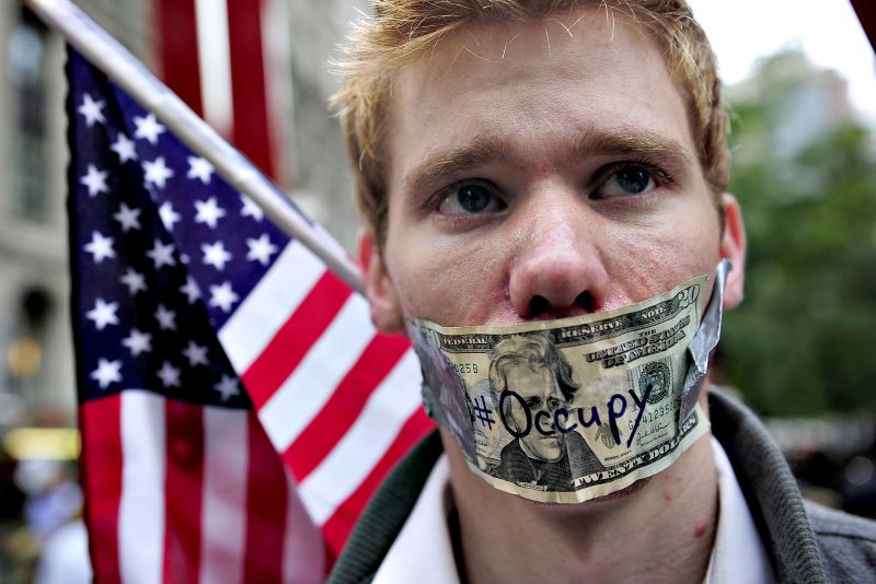 Manifestante usa nota de 20 dólares para protestar contra as corporações e o sistema financeiro, próximo a Wall Street, em Nova York | Emmanuel Dunand/AFP
