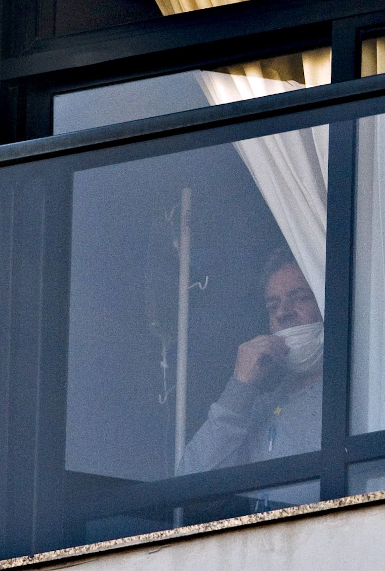 Lula aparece de máscara e ao lado de suporte para medicamento na janela do apartamento dele em São Bernardo do Campo: efeitos da quimioterapia | Diego Padgurschi/ Folahapress
