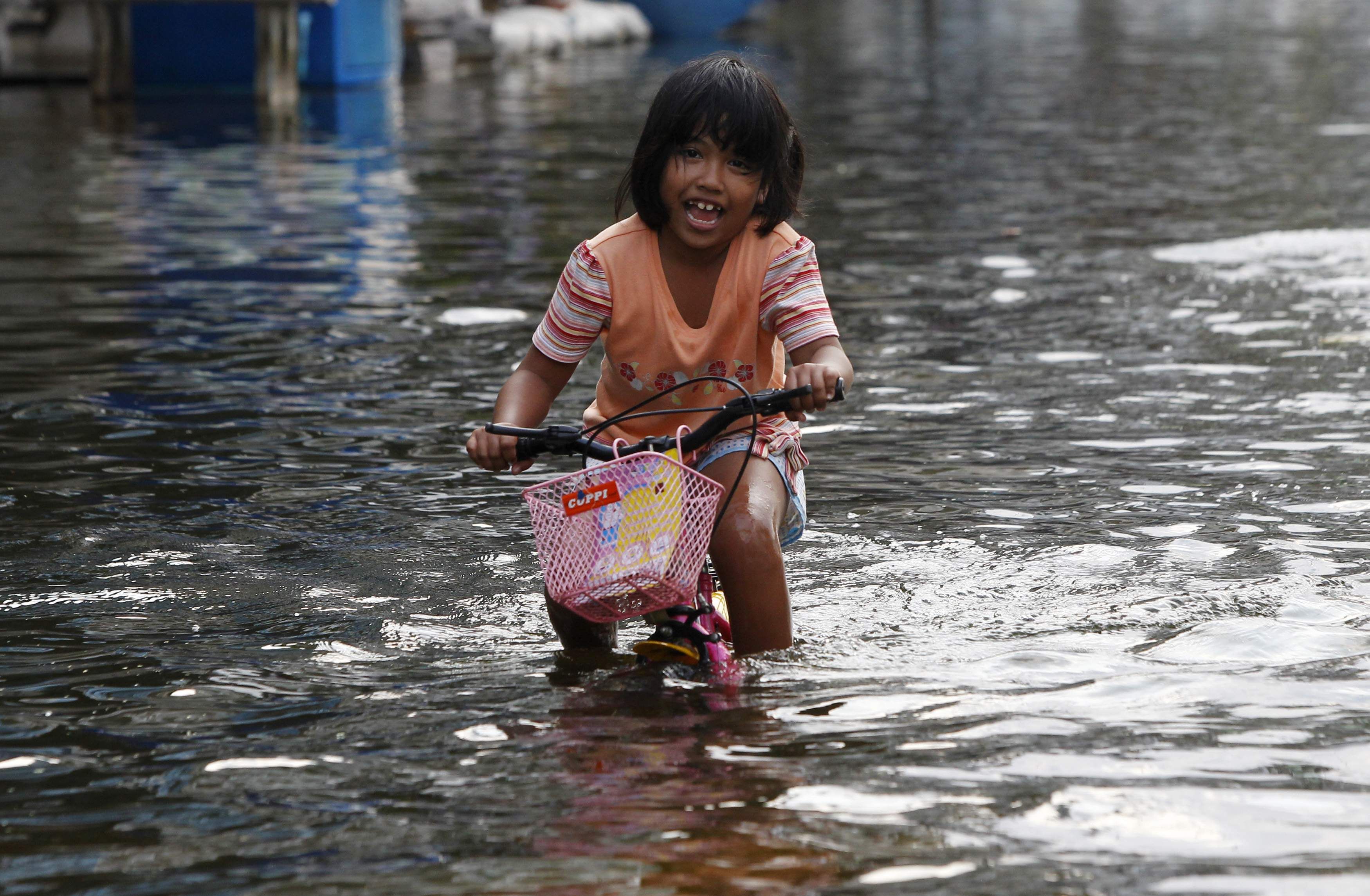 Menina anda de bicicleta por rua alagada, nos arredores de Bangcoc, na Tailândia | REUTERS/Chaiwat Subprasom