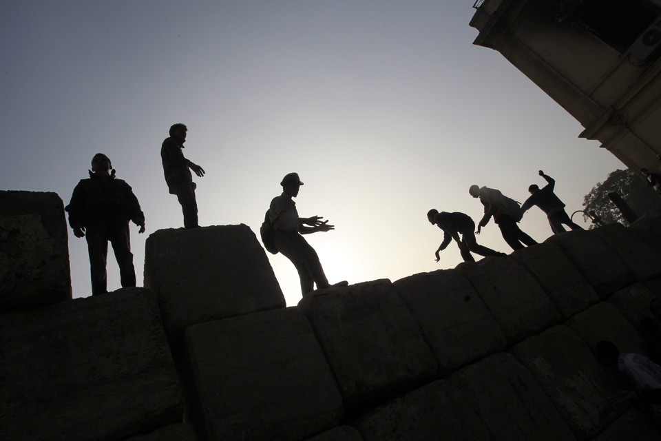 Jovens egípcios sobem em muro erguido pelas forças de segurança no Cairo. Confrontos entre manifestantes e polícia entram no quarto dia | AFP PHOTO/MOHAMMED ABED
