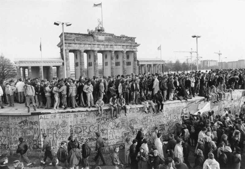 Minutos antes de o muro de Berlim ser derrubado, em 1989, os estudantes sobem a construção: ao fundo, o portão de Brandemburgo | Reprodução