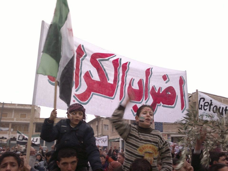 Crianças gritam palavras de ordem contra o presidente Assad durante manifestação nas ruas de Adlb, na Síria | REUTERS/Handout