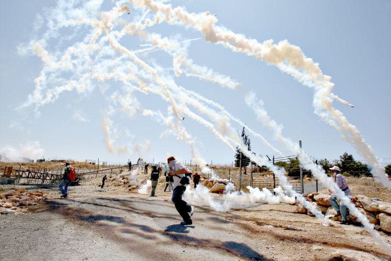 Manifestante palestino corre para escapar de bombas de gás lacrimogênio durante um protesto contra israelenses na vila de Bilin, perto de Ramallah, em 2009 | Abbas Momani/AFP