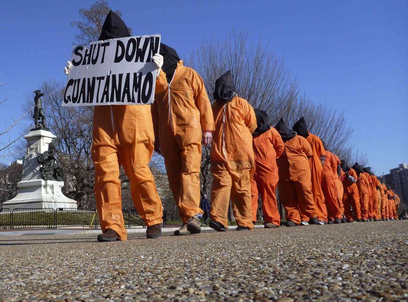 Ativistas vestidos como prisioneiros carregam cartaz pedindo o fechamento da prisão de Guantánamo | Larry Downing/Reuters