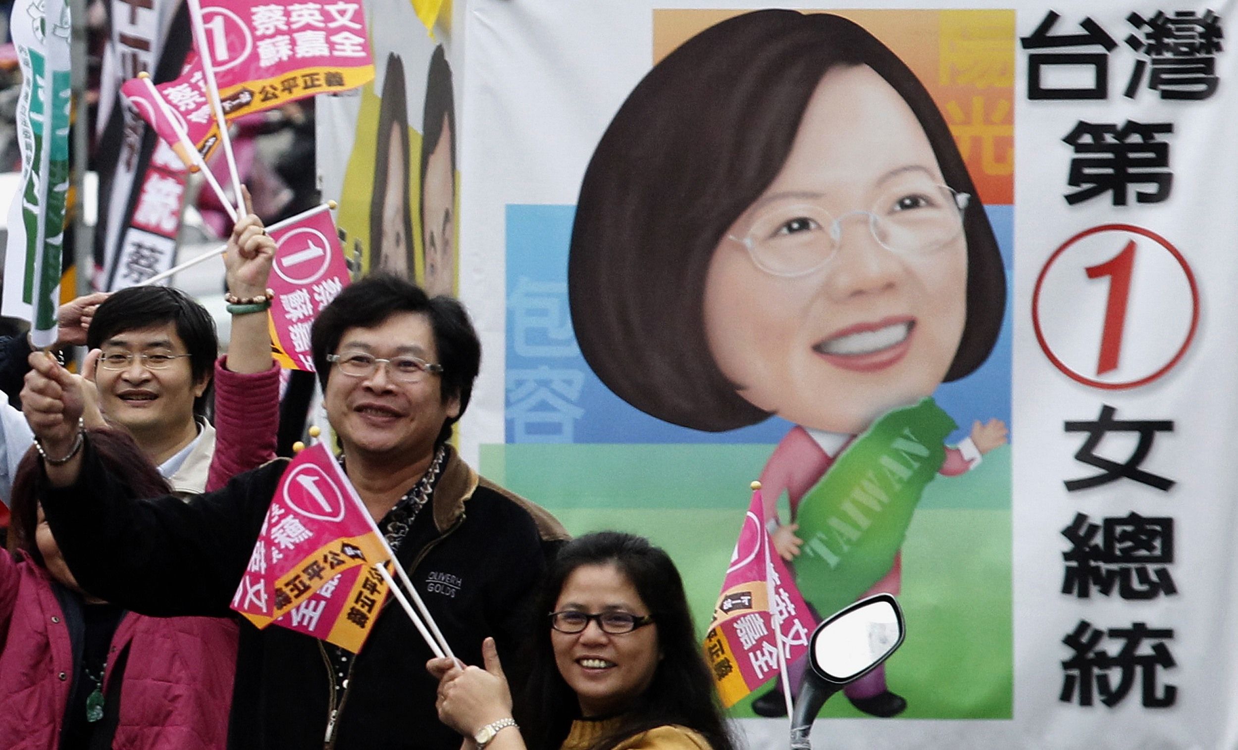 Simpatizantes do Partido Democrático Progressista e da cancidata à Presidência Tsai Ing-wen, acenam ao lado de imagem caricaturizada da candidata e da inscrição "A primeira mulher presidente do Taiwan", nas ruas de Taipei | REUTERS/Pichi Chuang