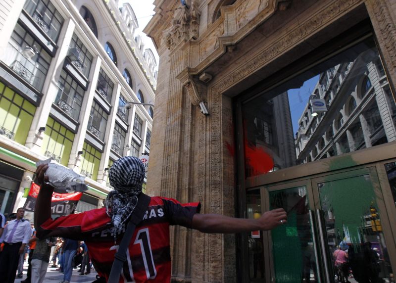 Homem mascarado, vestindo camisa do Flamengo, atira tinta contra a sede do banco HSBC, em Buenos Aires, Argentina: protesto contra a visita do príncipe William às ilhas Malvinas | Marcos Brindicci/Reuters