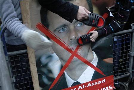 Manifestantes batem na imagem do presidente Bashar al-Assad com sapatos durante um protesto contra o regime de Assad do lado de fora da embaixada síria, em Londres. As forças do presidente sírio, tentando forçar a submissão da cidade de Homs, mataram nesta quarta-feira mais 19 pessoas, incluindo dois jornalistas ocidentais | REUTERS/Luke MacGregor