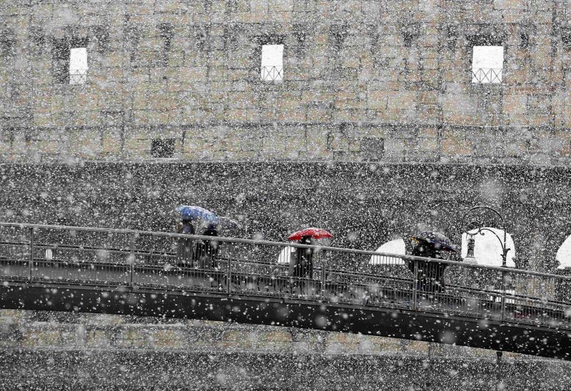 Pessoas se protegem da neve com guarda-chuvas enquanto caminham por uma ponte em frente ao Coliseu, em Roma | REUTERS/Alessandro Bianchi