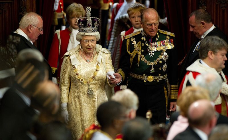 Elizabeth II segura a mão de seu marido, o príncipe Philip, duque de Edimburgo, quando chega para dirigir a Câmara dos Lordes, durante o Estado de Parlamento Aberto em Westminster, centro de Londres | AFP PHOTO / POOL / LEON NEAL