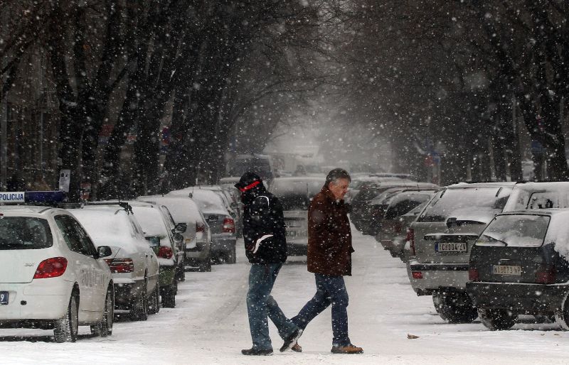 Homens atravessam a rua embaixo de neve e enfrentam temperaturas baixíssimas em Nis, na Sérvia | AFP PHOTO / SASA DJORDJEVIC