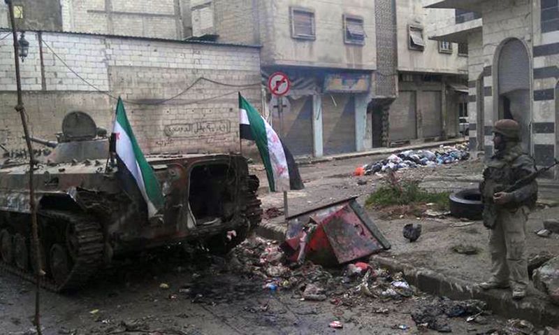Rebelde sírio flagrado ao lado de um veículo militar destruído em Homs, na região central do país, onde mais de 200 pessoas teriam morrido em confrontos com as forças do presidente Bashar al-Assad | LCC/AFP/Divulgação