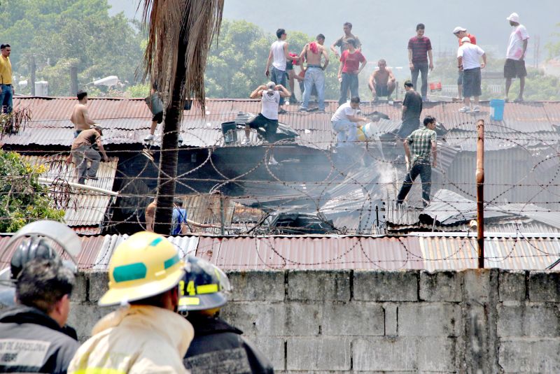 Detentos ocupam o telhado da prisão enquanto outros tentam apagar o fogo em San Pedro Sula, no norte de Honduras | Carlos Perez/AFP