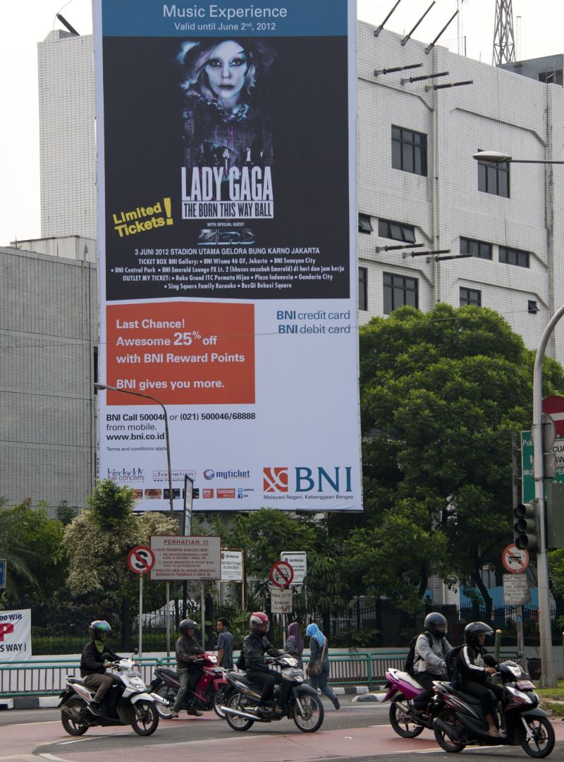 Motoristas indonésios passam por outdoor que anuncia show de Lady Gaga no país | AFP PHOTO / OSCAR SIAGIAN