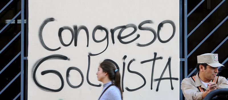 Mulher caminha em frente à placa que acusa congresso paraguaio de golpe | AFP PHOTO/Norberto DUARTE