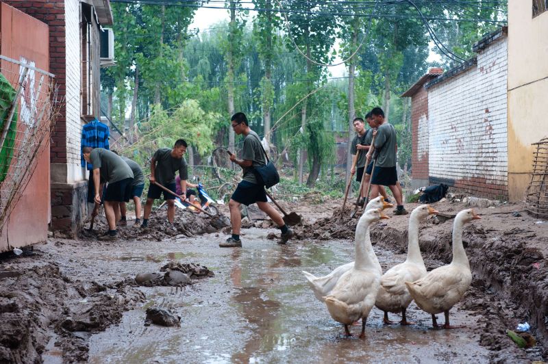 Homens tentam limpar a lama que toma conta das ruas de Pequim, na China | CHINA OUT AFP PHOTO