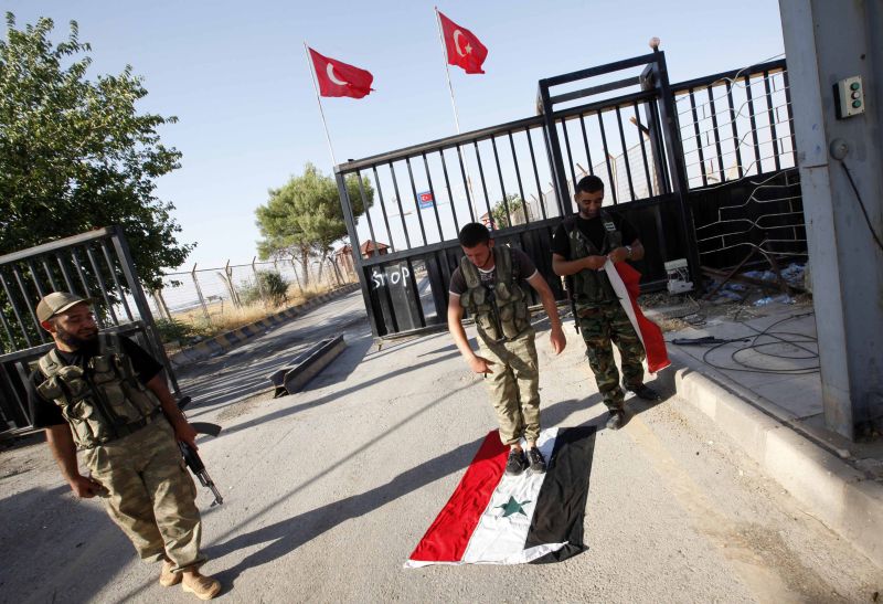 Membro do Expercito Livre da Síria pisa em bandeira do país na fronteira da Síria com a Turquia | REUTERS/Umit Bektas