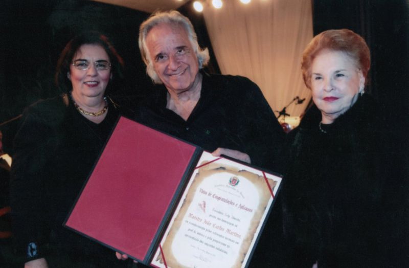 No Castelo do Batel, o maestro João Carlos Martins recebeu da vereadora Nely Almeida (à direita) Comenda da Câmara Municipal de Curitiba, proposição dela, que exalta sua carreira musical, em ato testemunhado pela igualmente vereadora Julieta Reis | Divulgação