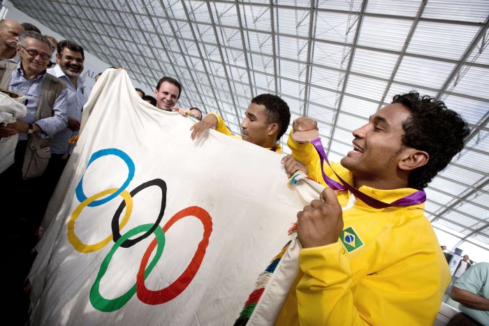 Os irmãos Falcão, medalhistas no boxe, seguram a bandeira olímpica no Aeroporto do Galeão, no Rio de Janeiro | Virginie Valdois / AFP