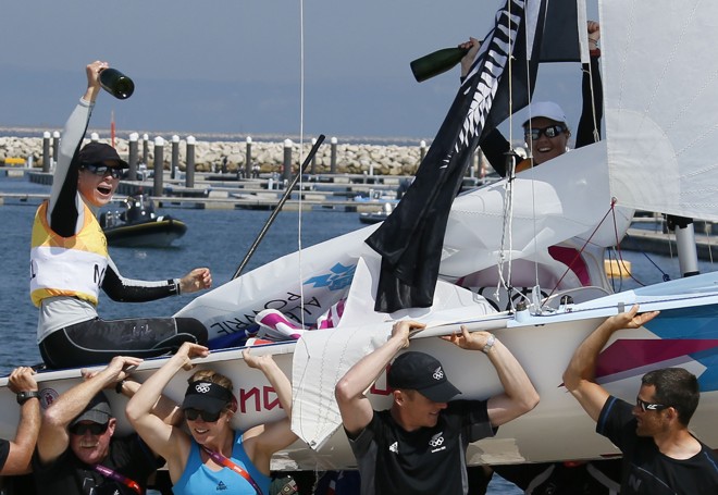 Garrafas de champanhe nas mãos, as neozelandesas Jo Aleh e Olivia Powrie saem carregadas do mar após a conquista do ouro na classe 470 da vela | 