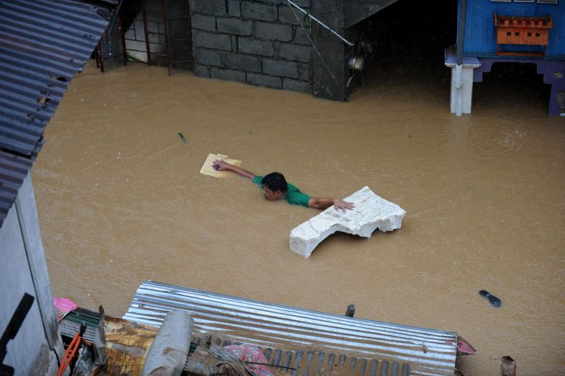 Homem tenta cruzar área alagada com um flutuante em Manila, capital das Filipinas | AFP Photo/Noel Celis