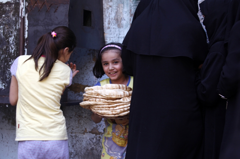 Garota sorri com uma pilha de pães comprados em uma padaria de um distrito de Aleppo | Zain Karam/Reuters