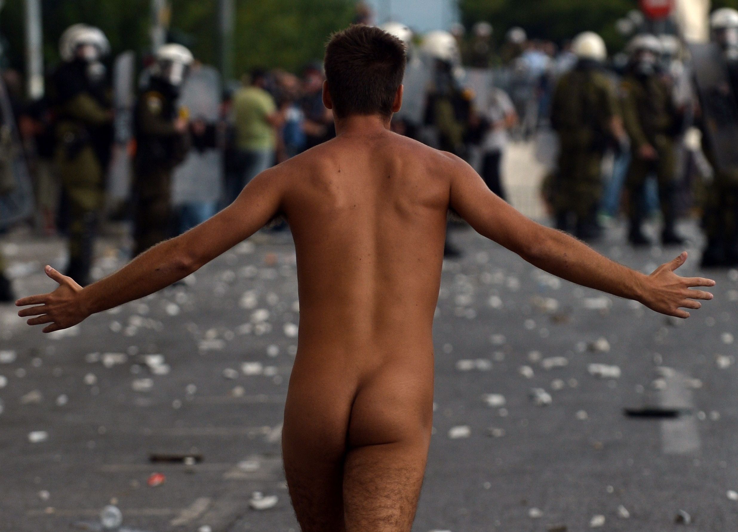 Homem pelado corre por uma rua de Atenas em protesto contra a visita da chanceler alemã Angela Merkel à Grécia nesta terça-feira | AFP PHOTO /ARIS MESSINIS