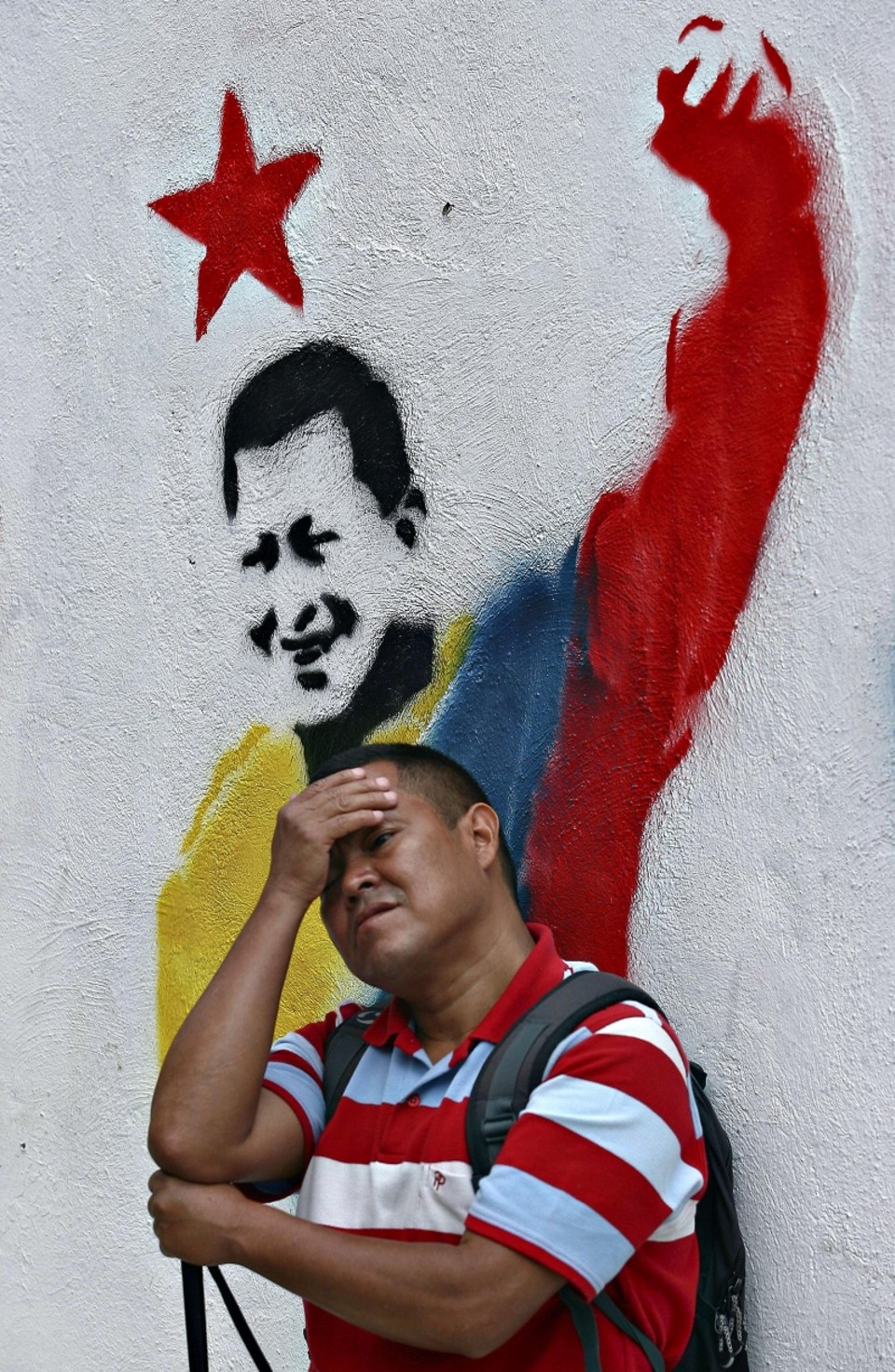 Homem se escora em parede com graffiti do presidente Chávez | Geraldo Caso/AFP