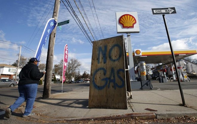 Mulher caminha por posto com placa indicando que a gasolina acabou, em Staten Island | Mike Segar/Reuters