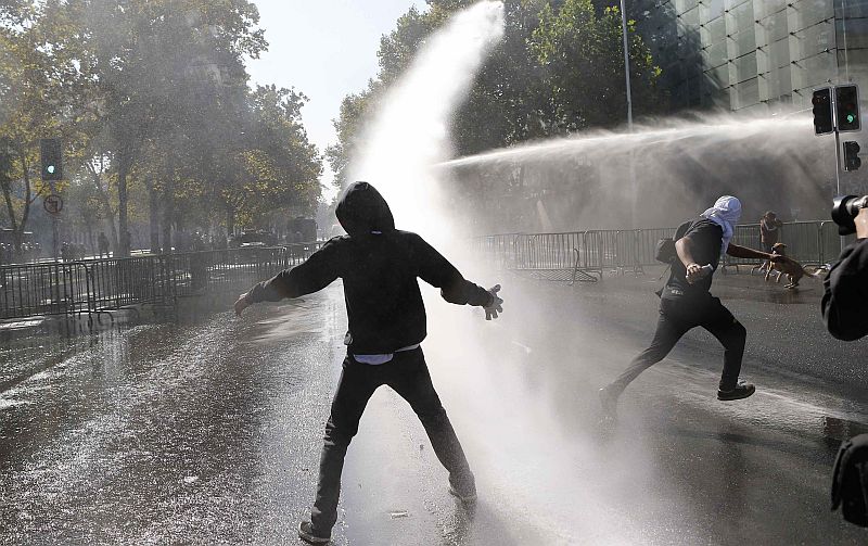 Manifestantes enfrentam os jatos de água da polícia usados para dispersar os protestos em Santiago, no Chile. | REUTERS/Ivan Alvarado