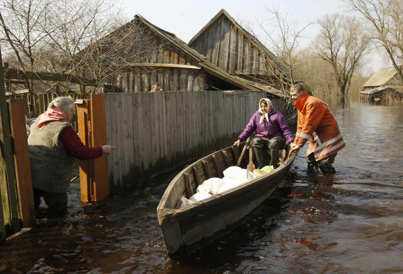 Um trabalhador de resgate ajuda moradores a deixam suas casas após a água do rio Stviga transbordar na vila de Ozerany, cerca de 270 km ao sul de Minsk, na Bielorrússia | REUTERS / Vasily Fedosenko