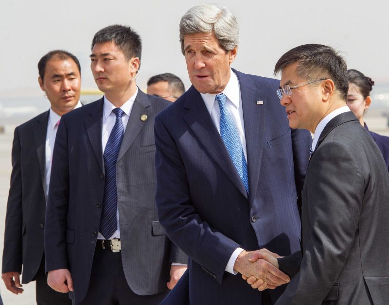 O secretário de Estado norte-americano, John Kerry, aperta mãos com o embaixador americano na China, Gary Locke, durante chegada no aeroporto de Pequim | Reuters