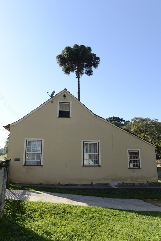 Características da arquitetura do Vêneto na casa em Curitiba: paredes grossas, feitas sem tijolos; formato do telhado e das janelas; cruz como enfeite e arquitetura simples |