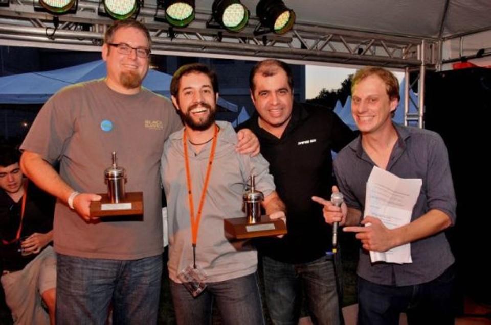 O mineiro Kevin Figueiredo (com o caneco pendurado no pescoço) foi o vencedor do concurso nacional de cervejas artesanais. A competição ocorreu durante o VIII Encontro Nacional das Associações dos Cervejeiros Artesanais, realizado sábado na fábrica da Way Beer, em Pinhais. O prêmio foi entregue pelo norte-americano Tom Schmidlin (à esq.). Também na foto, o presidente da Associação de Cervejeiros do Paraná, Anuar Tarabai (de preto), e o humorista Fagner Zadra, mestre-de-cerimônias da festa | Bruno Volcov