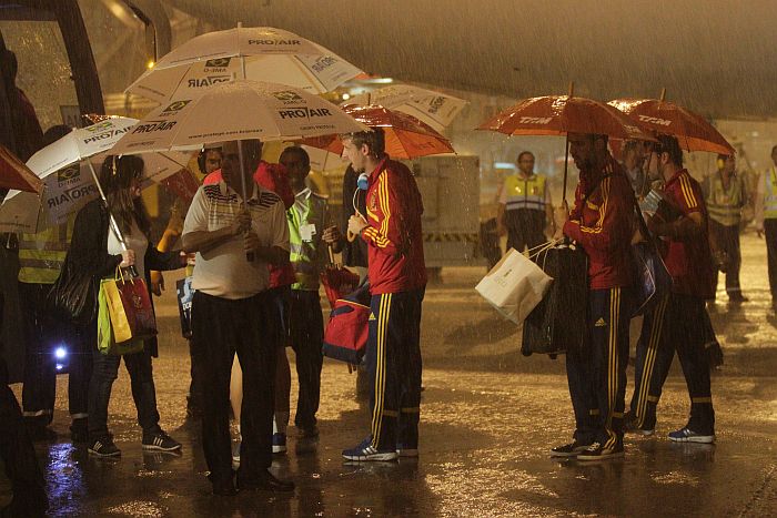 Jogadores da Espanha tiveram de apelar aos guarda-chuvas no desembarque em Recife | Rodrigo Lôbo / Folhapress