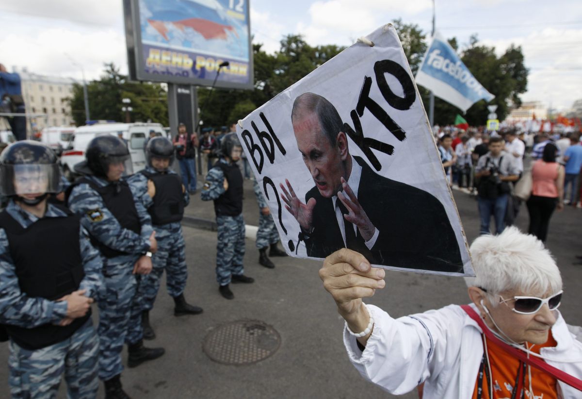 Senhora segura cartaz onde lê-se "Quem é você?" com uma foto do presidente russo, Vladimir Putin | Reuters/Sergei Karpukhin