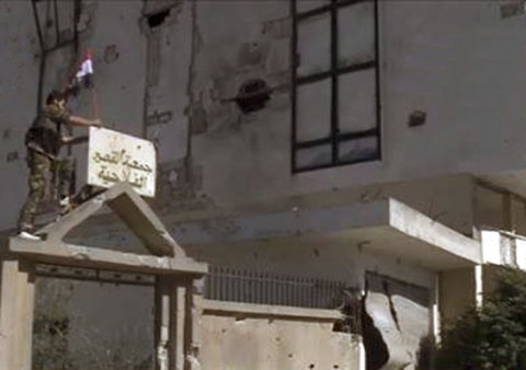 Regime sírio retoma controle da estratégica cidade de Al Qusair Soldado coloca uma bandeira do regime sírio no topo de um prédio em Al Qusair | Reuters/Sana/Divulgação