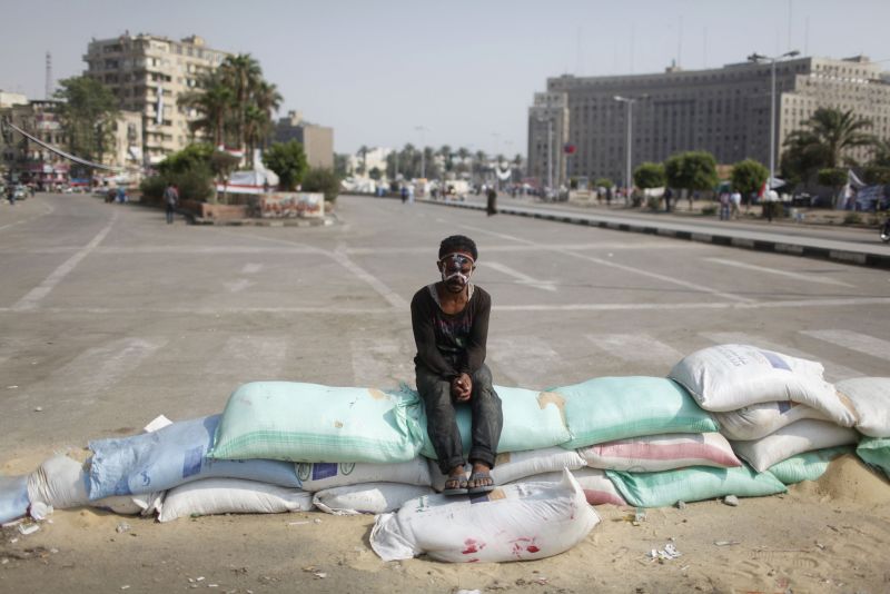 Sacos de areia usados para fazer uma barricada na Praça Tahrir servem de banco para um manifestante de rosto pintado com as cores da bandeira do Egito | Asmaa Waguih/Reuters